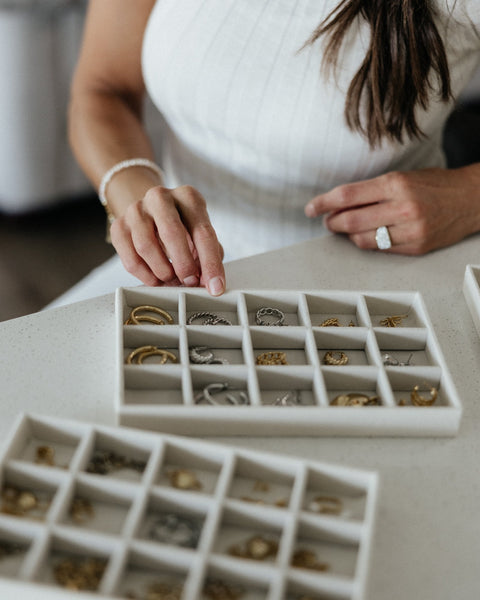 Hands sorting jewelry in a white divided tray on a wooden table